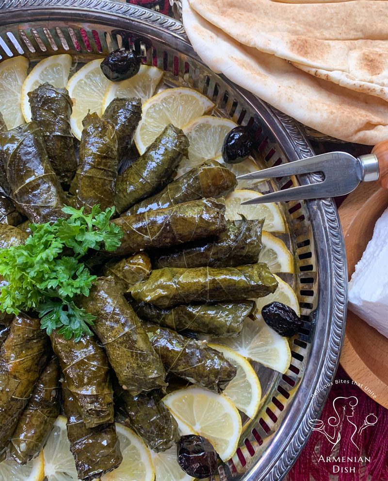 A silver platter of Armenian dolma, grape leaves stuffed and rolled, with lemon slices, olives, parsley and flatbread