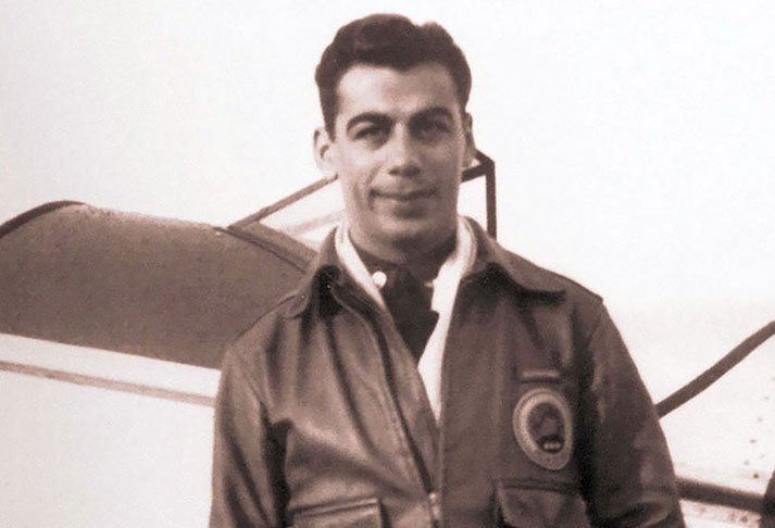 A young Kirk Kerkorian in a leather flight jacket standing in front of an airplane